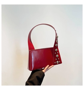 Detail of red patent leather underarm bag featuring distinctive silver spherical studs