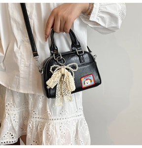 Détail d'un mini sac à main noir texturé avec un écusson de chien et un gri-gri en perle