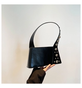 Detailed close-up of glossy black leather bag featuring industrial silver stud accents