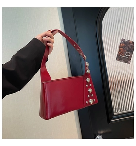 Detail of red patent leather underarm bag with decorative silver metal studs