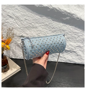 Close-up of light blue denim cylinder bag with silver metal studs and chain strap