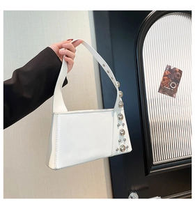 Close-up of stylish white leather shoulder bag with silver stud details and punk aesthetic