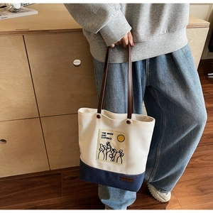 Close-up of a two-tone canvas tote bag with leather handles and artistic illustration