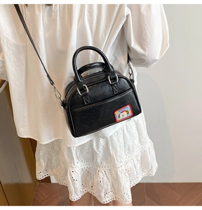 Détail du mini sac Boston noir en cuir avec écusson chiot ludique et bandoulière fine