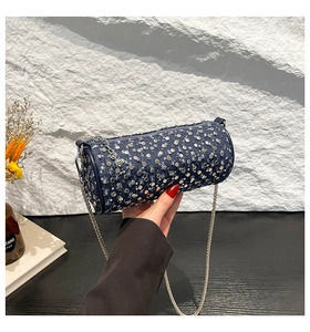 Detail of blue denim cylindrical bag featuring silver rivets and metal chain strap