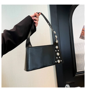 Detail of a black rectangular underarm bag with silver studs and polished faux leather