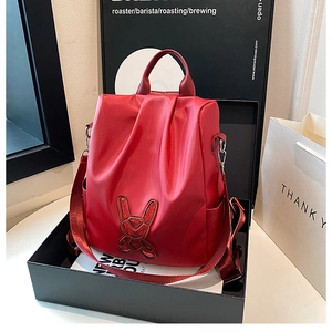 Detail of red nylon backpack featuring a mirror rabbit patch and top leather handle