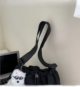 Detail of black drawstring tote bag with plush puppy pendant and wide nylon strap