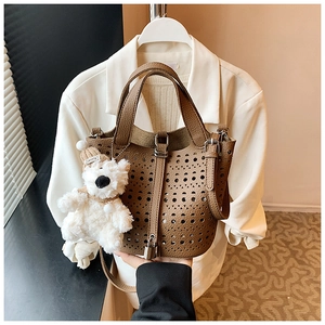 Détail du sac seau marron découpé au laser en cuir grainé avec un petit ours en peluche