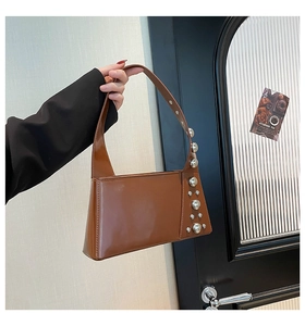 Detailed shot of brown glossy leather shoulder bag featuring vintage silver rivet studs