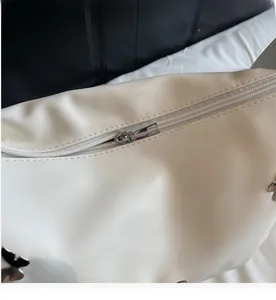 Gros plan sur la fermeture éclair argentée et papillon d'un sac en cuir blanc plissé