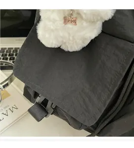 Detail of black nylon messenger bag with buckle closure and plush dog charm accessory