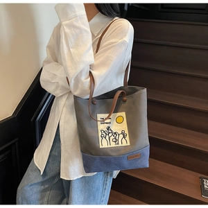 Detail of canvas tote bag showing grey and blue color block design and leather handles