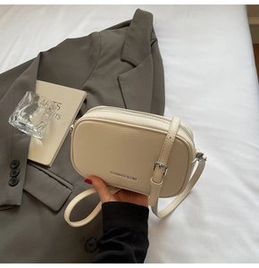 Détail du sac à bandoulière en cuir blanc cassé avec logo et fermeture à glissière
