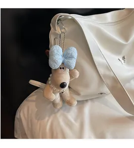 Détail d'un pendentif en peluche beige avec nœud bleu et perles sur un sac blanc