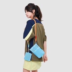 Detail of light blue mesh crossbody bag with vibrant orange and black woven rope strap