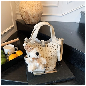 Détail du sac seau ajouré crème avec charm ours mignon posé sur des livres