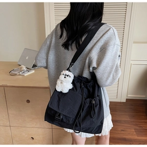 Detail of black nylon drawstring messenger bag with a white plush puppy charm decoration