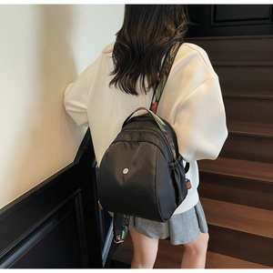 Vista posteriore di un mini zaino in nylon nero con spalline colorate in stile bohémien