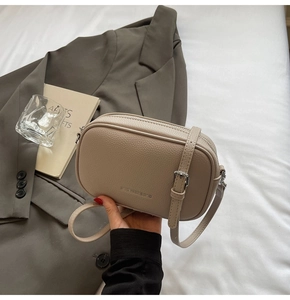 Détail du sac bandoulière en cuir beige grainé avec boucle argentée et logo de marque