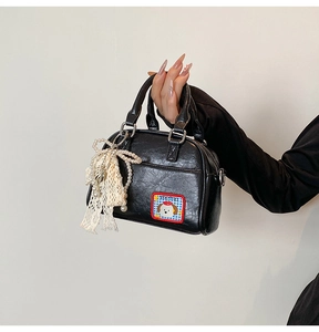 Détail du sac à main noir brillant avec écusson Trotro et pendentif noeud en perles