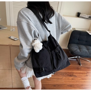 Detail view of black drawstring crossbody bag featuring a plush bear charm on the strap