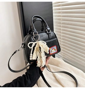 Détail du sac Boston noir avec écusson chien et breloque en perles et dentelle
