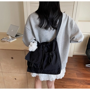 Detail view of black drawstring crossbody bag featuring textured fabric and plush charm