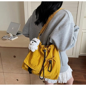 Detail of yellow canvas crossbody bag with drawstring pockets and white plush dog charm