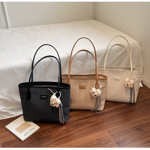 Three canvas tote bags in black, khaki, and cream with plush bear charms and tassels