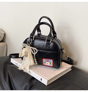 Détail du sac bowling en cuir verni noir avec écusson chiot et pendentif nœud en perles