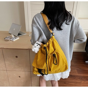 Detail of a bright yellow drawstring bucket bag with a plush charm on an adjustable strap