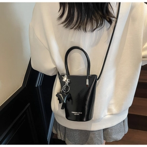 Detail of a black patent leather bucket bag with top handle and animal-shaped charm accessory