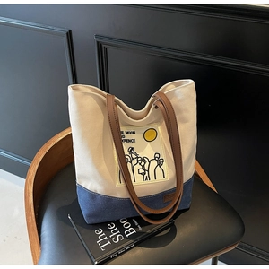 Detail of canvas tote bag showing off-white fabric and blue denim patchwork with brown straps