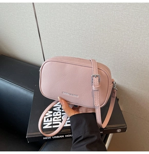 Sac bandoulière en cuir rose à grain litchi avec logo de la marque sur un livre
