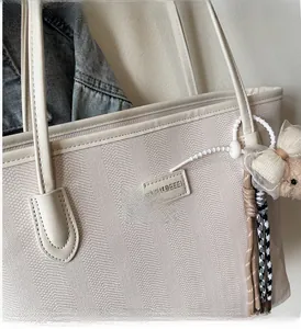 Close-up of beige tote bag with herringbone texture and cute bear charm decoration