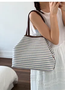 Blue and white striped canvas tote bag with leather straps shown on model in indoor setting