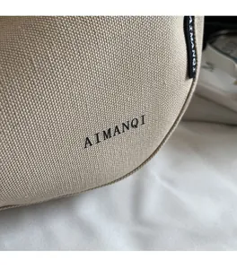 Nahaufnahme des beigen Strickstoffs der Umhängetasche mit AIMANQI Logo und Textur