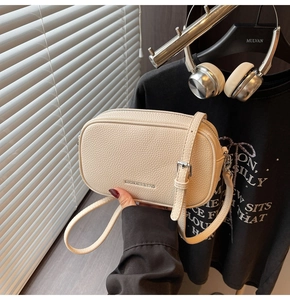 Gros plan du sac bandoulière en cuir grainé crème avec double fermeture éclair et métal