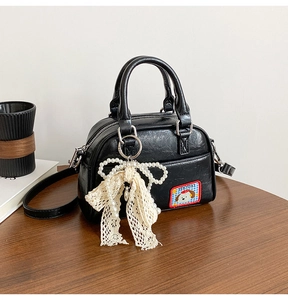 Détail du mini sac bowling noir brillant avec un nœud en dentelle et une perle