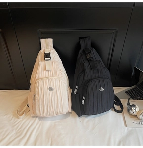 Detail shot of pleated crossbody bags in cream and black with stylish metal logo