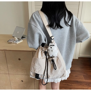 Detail of beige drawstring crossbody bag with plush puppy pendant and functional pockets