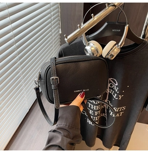 Détail du cuir grainé noir et du logo argenté sur ce sac bandoulière au style minimaliste
