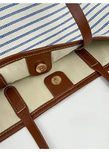 Detail of blue striped canvas tote bag with brown leather trim and magnetic gold closure