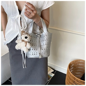 Détail d'un sac seau argenté ajouré avec un charm ours en peluche et un fermoir métallique