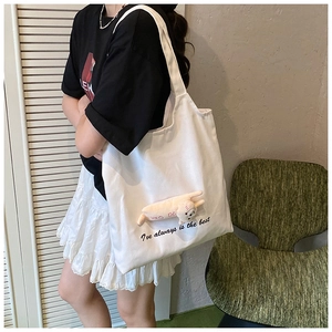 Detail of white canvas tote bag featuring cute plush animal charm and slogan print