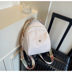 Zaino in nylon beige con tracolla etnica intrecciata posizionato su una valigia