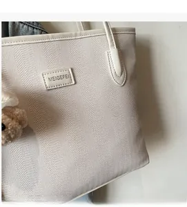 Detail of herringbone fabric tote bag with a brown teddy bear charm and leather tag