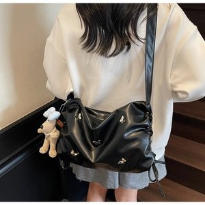 Détail du sac bandoulière plissé noir avec nœuds argentés et breloque chiot