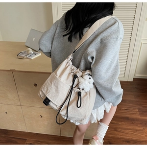 Detail of off-white drawstring crossbody bag with side pocket and plush dog charm
